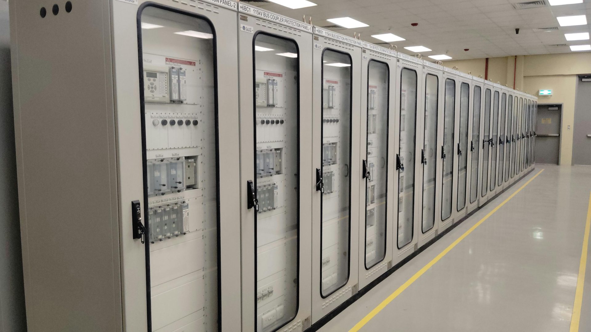 View of an industrial control room featuring rows of electrical panels in a well-lit environment.